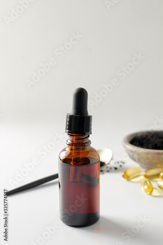 Obraz na płótnie Glass bottle and pills of black cumin seeds essential oil. Nigella Sativa in spoon and bowl on white background w salonie
