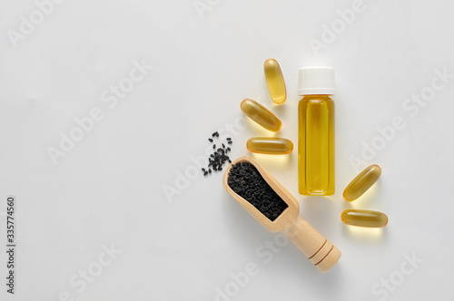 Bottle and pills of black cumin seeds essential oil. Nigella Sativa in wooden spoon on white background