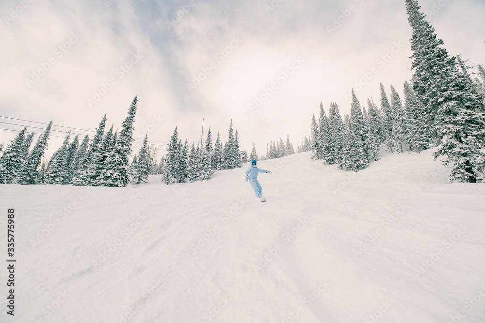 Freerider female snowboarder wearing snowboard jumpsuit riding in winter snow-covered forest in ski resort