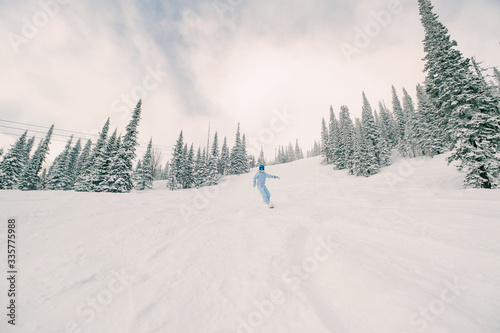 Freerider female snowboarder wearing snowboard jumpsuit riding in winter snow-covered forest in ski resort © Annatamila