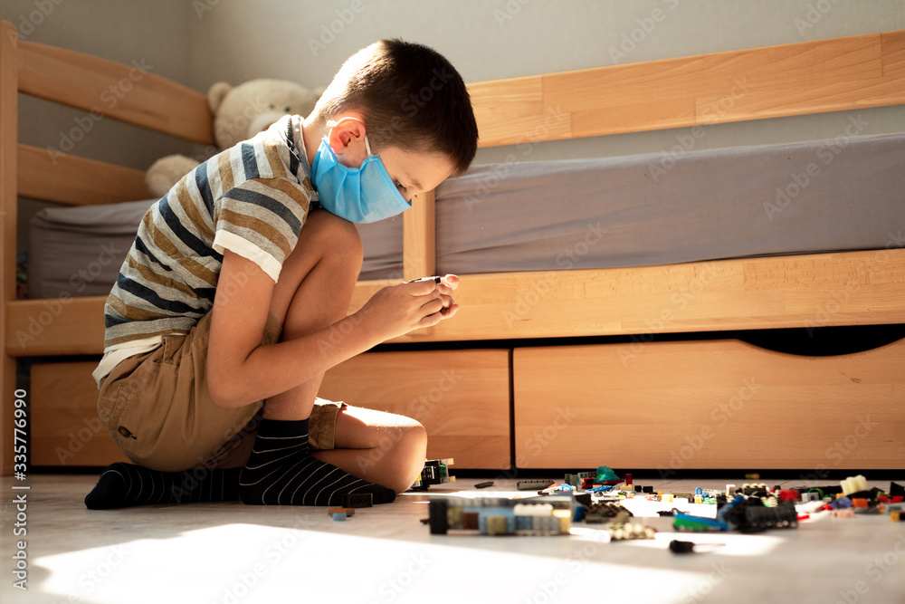 Stay at home quarantine coronavirus pandemic prevention. A boy in a protective medical mask plays and folds the constructor himself in his room. Prevention epidemic. COVID-19. Stay at home quarantine coronavirus pandemic prevention. A boy in a protective medical mask plays and folds the constructor himself in his room. Prevention epidemic. COVID-19.