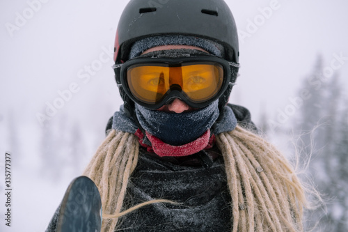 Portrait of snowboarder with board wearing mask in snowy winter landscape outdoors