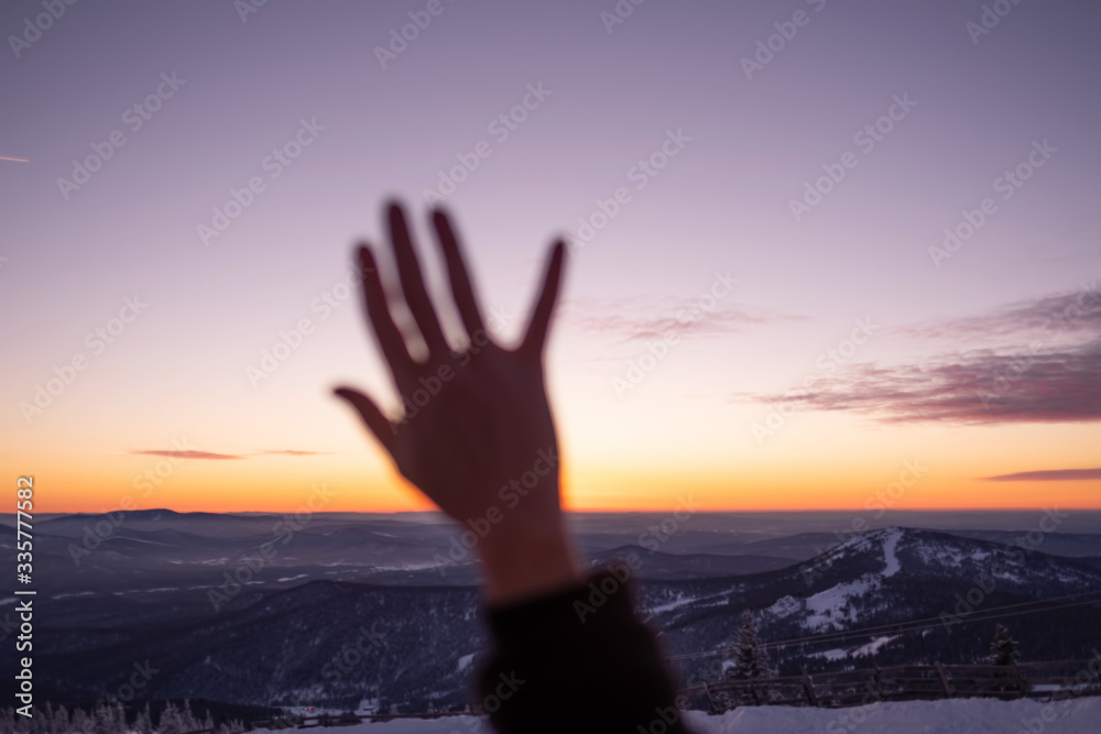 Female hand out of focus on mountains landscape and sunset sky background