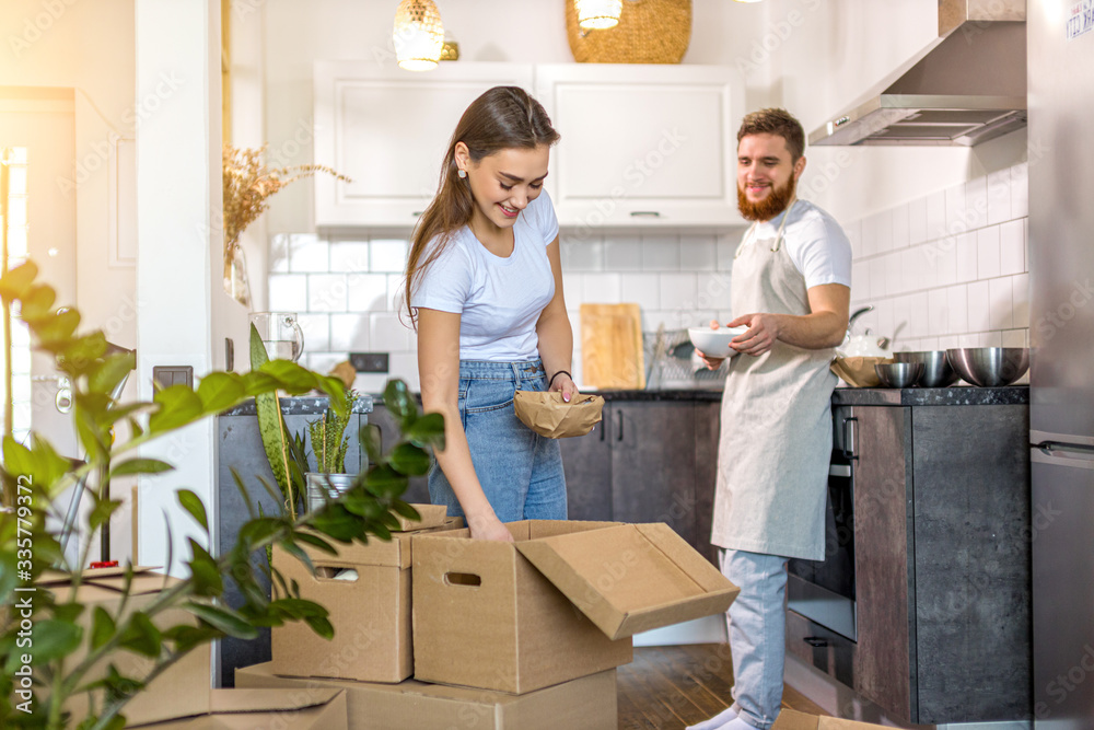 young caucasian married couple moved to a new house, they unpack boxes at home together. couple in domestic clothes young caucasian married couple moved to a new house, they unpack boxes at home together. couple in domestic clothes