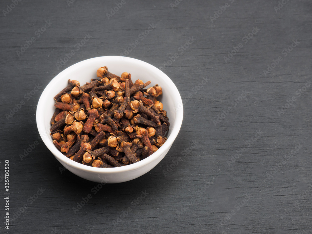 Spice cloves in white ceramic bowl on black wooden background. Healthy eating and organic food concept Spice cloves in white ceramic bowl on black wooden background. Healthy eating and organic food concept