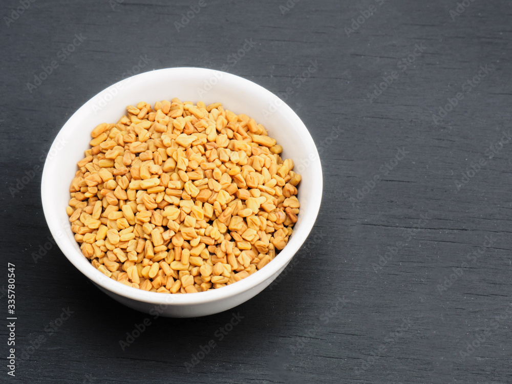 Spice fenugreek in white ceramic bowl on black wooden background. Healthy eating and organic food concept Spice fenugreek in white ceramic bowl on black wooden background. Healthy eating and organic food concept