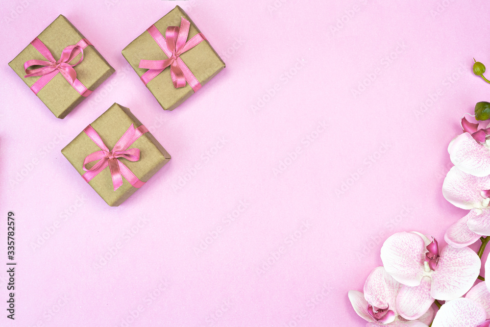 flat-lay of present gift boxes with pink ribbon on pink background with orchid flowers. spring concept. Copy space