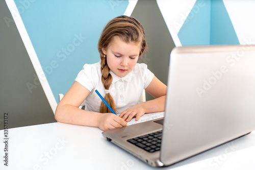 Distance learning online education. Schoolgirl studying at home with digital tablet laptop notebook and doing school homework. Sitting at the table with training books
