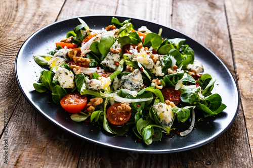 Fresh salad - blue cheese, cherry tomatoes, vegetables and walnuts on wooden background