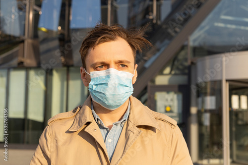 Handsome young European man in spring clothes on the street with a medical mask on his face. Closeup portrait of a man in a respirator to protect against infection with influenza virus or coronavirus