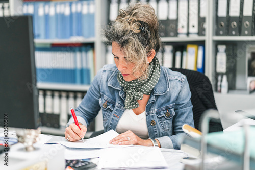 Mujer escribiendo en un papel en una oficina con archivadores de fondo.