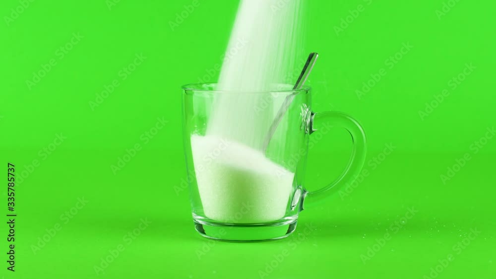 Pour sugar mug glass tea spoon thick bottom green contrasting background concept Pour sugar mug glass tea spoon thick bottom green contrasting background concept