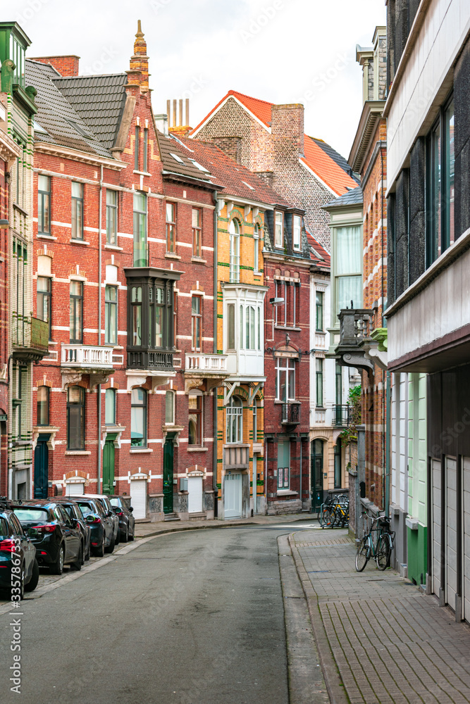 A street without people, with cars and bicycles. Colourful brick buildings in Ghent, Belgium, during the day. Concept of travel and real estate.
