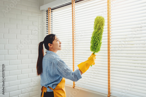 Young asian woman cleaning house wiping dust using Feather broom and duster while cleaning on window House keeping concept photo