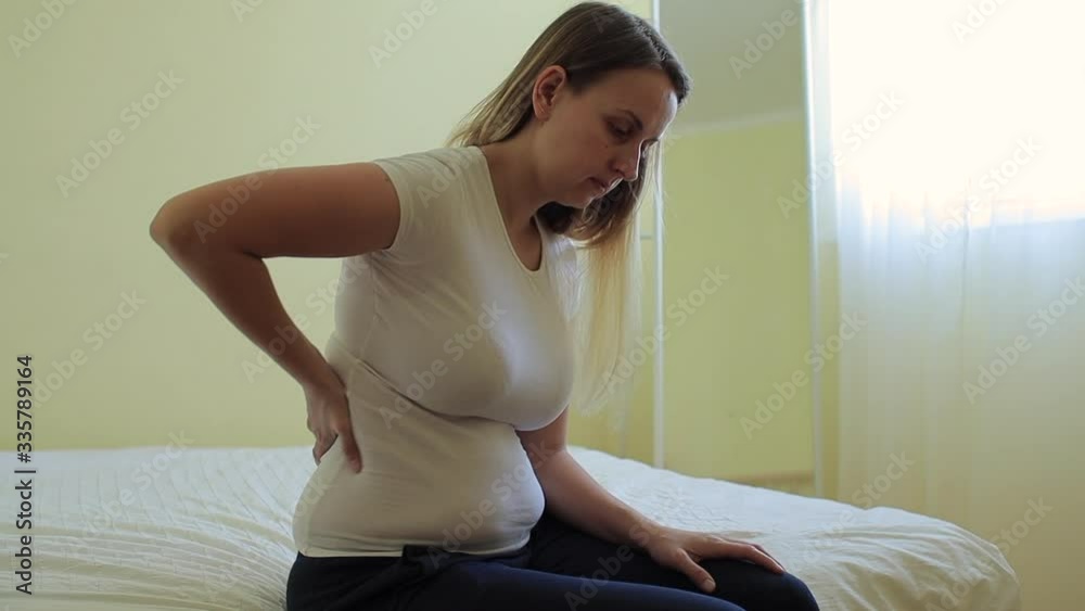 Young plump woman sitting in bedroom with backache