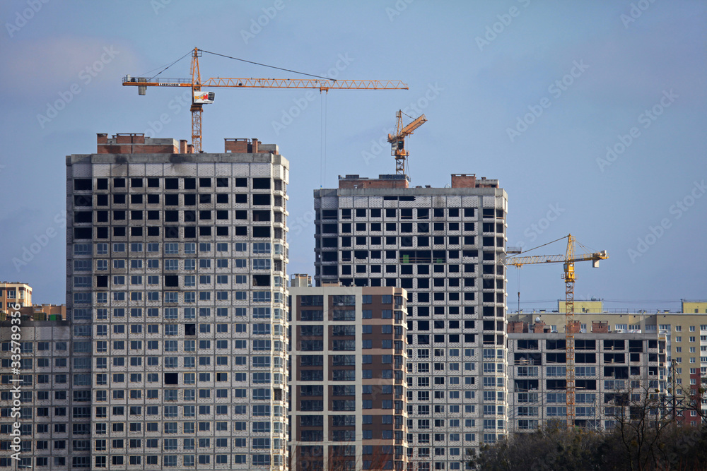 High-rise construction cranes and array of buildings under construction on the blue sky background. Building construction site with cranes. The construction of multifamily modern apartment buildings 