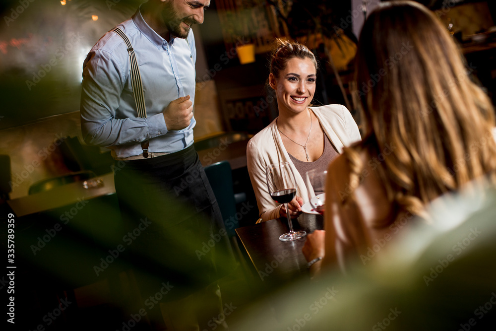 Smiling young female friends at a restaurant with waiter serving dinner