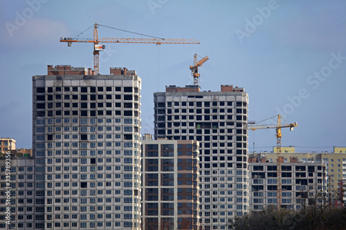 High-rise construction cranes and array of buildings under construction on the blue sky background. Building construction site with cranes. The construction of multifamily modern apartment buildings 