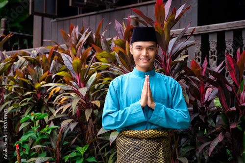 A portrait of young malay man in his traditional teal cloth, samping songket and songkok. Selamat Hari Raya gesture