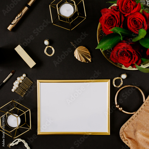 Golden blank frame with luxury golden accessories for women's beauty. Dating concept with red lipstick, roses, golden chain, earrings and handbag on black background. Elegant modern template for