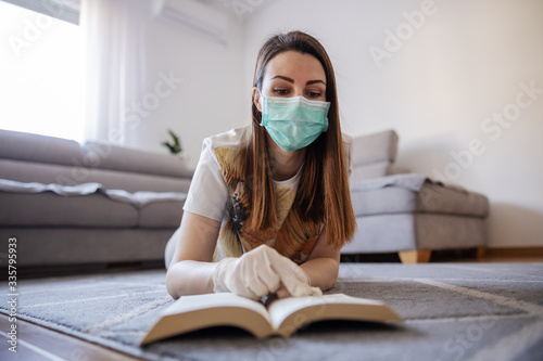 Woman in home isolation wearing face mask and gloves, reading a book and studying information about coronavirus outbrake 2020. Home education during quarantine. photo