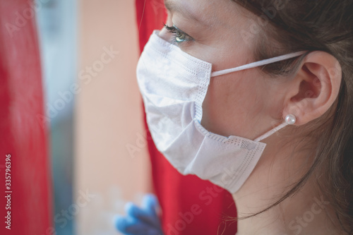 Fototapeta Naklejka Na Ścianę i Meble -  young woman wearing a surgical mask looking through the window