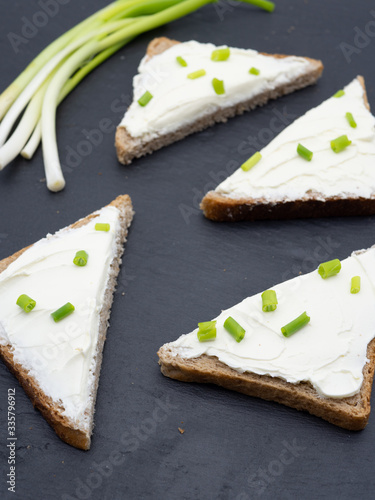 slices of bread with cream cheese spread and fresh 
green onion on black slate breakfast shack concept