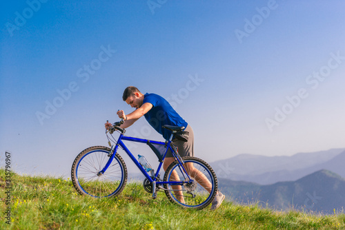 Fit male mountain biker pushing his bike uphill while looking exhausted on a sunny summer day.