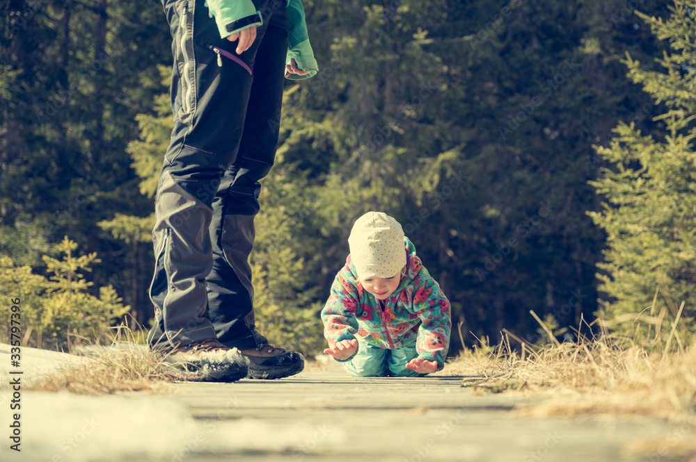 Naklejka premium Cute girl crawling on a boardwalk in running through winter forest.