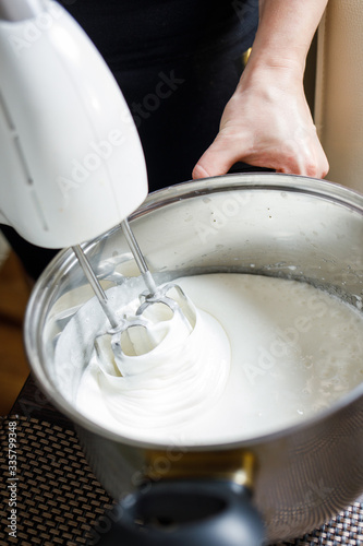 Woman whisking with mixer eggs whites with sugar