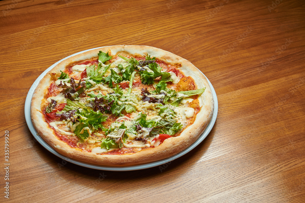 Appetizing baked Italian pizza with cream sauce, lettuce, chicken and parmesan on a white plate on a wooden background. Pizza caesar Appetizing baked Italian pizza with cream sauce, lettuce, chicken and parmesan on a white plate on a wooden background. Pizza caesar