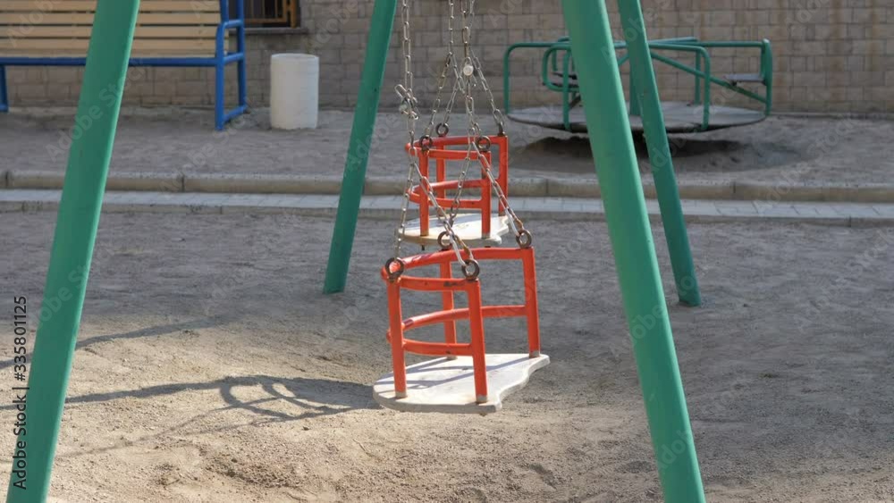 Empty swings on playground swaying in wind Empty swings on playground swaying in wind