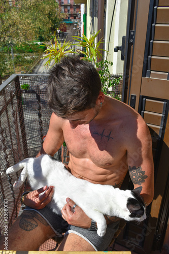 Man sitting in the sun on the balcony with his cat in his arms.