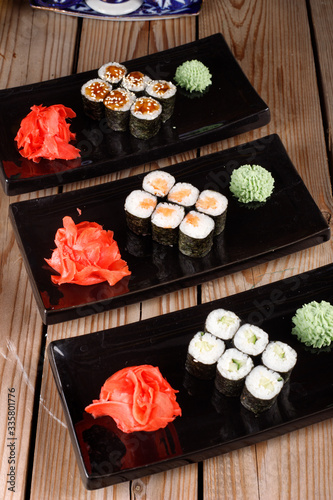 Set of baked sushi rolls with wasabi and ginger on a black background.