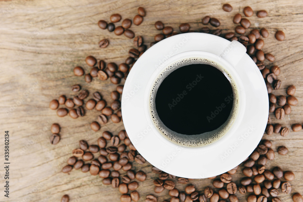 Coffee cup and coffee beans on table / black coffee in white mug on wooden background Coffee cup and coffee beans on table / black coffee in white mug on wooden background