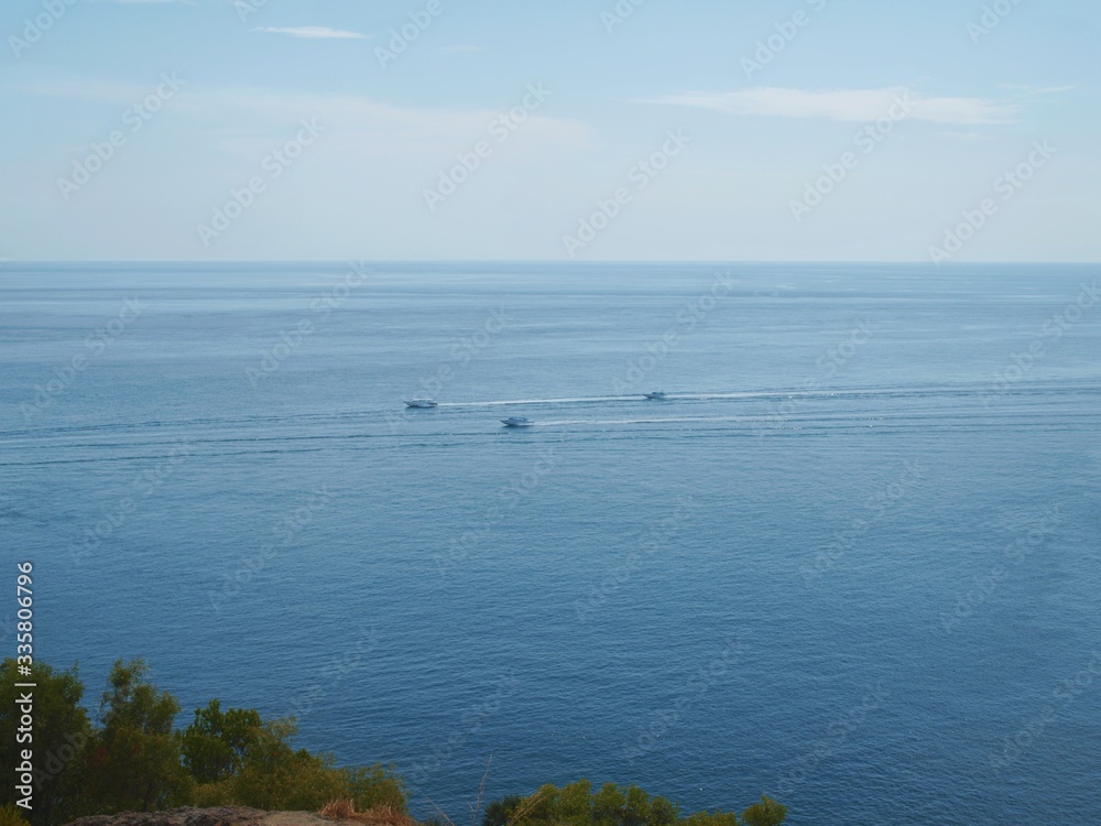 Three speedboats moving on the sea surface. View from the coast from the hill. Wild shore with forest. Panorama of ocean and rushing motor boats with high speed. Seascape in good weather. 