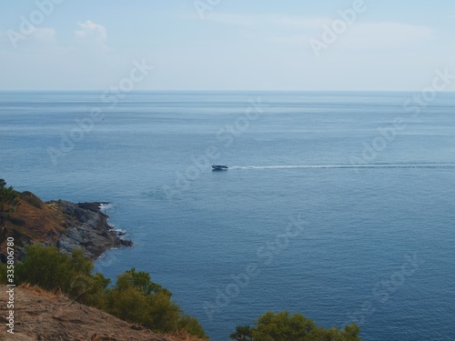 Seascape - rocky coast, expanse of water, horizon line and speeding boat rushing across the sea surface. Tropical island shore, cliff and ocean - panoramic view.
