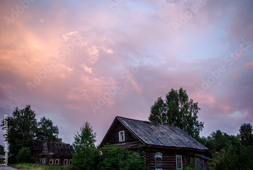 Sunset in the village. Bright beautiful sky over a wooden house and a blooming field. © Tatiana Dragunova