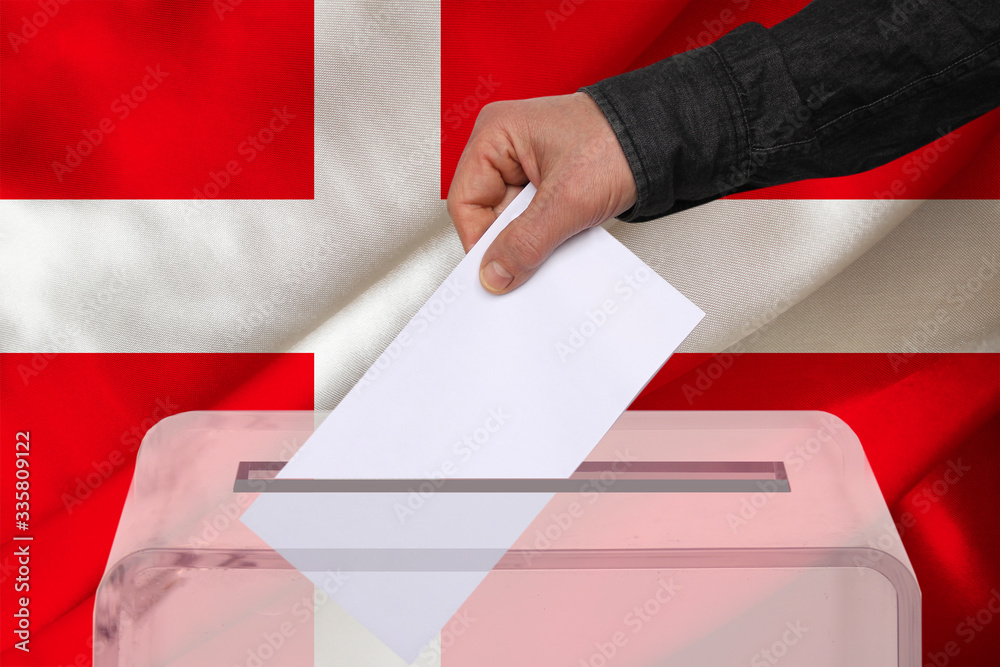 male voter drops a ballot in a transparent ballot box against the background of the national flag of Denmark, concept of state elections, referendum male voter drops a ballot in a transparent ballot box against the background of the national flag of Denmark, concept of state elections, referendum