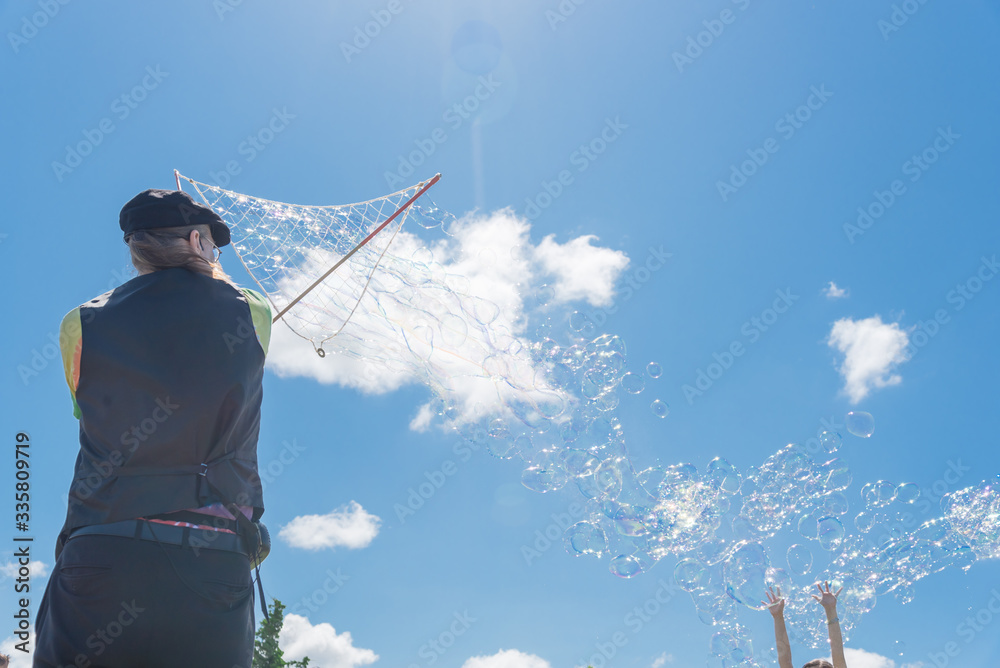 Rear view bubbles maker artist making giant bubble with kid rising hands in American park Rear view bubbles maker artist making giant bubble with kid rising hands in American park