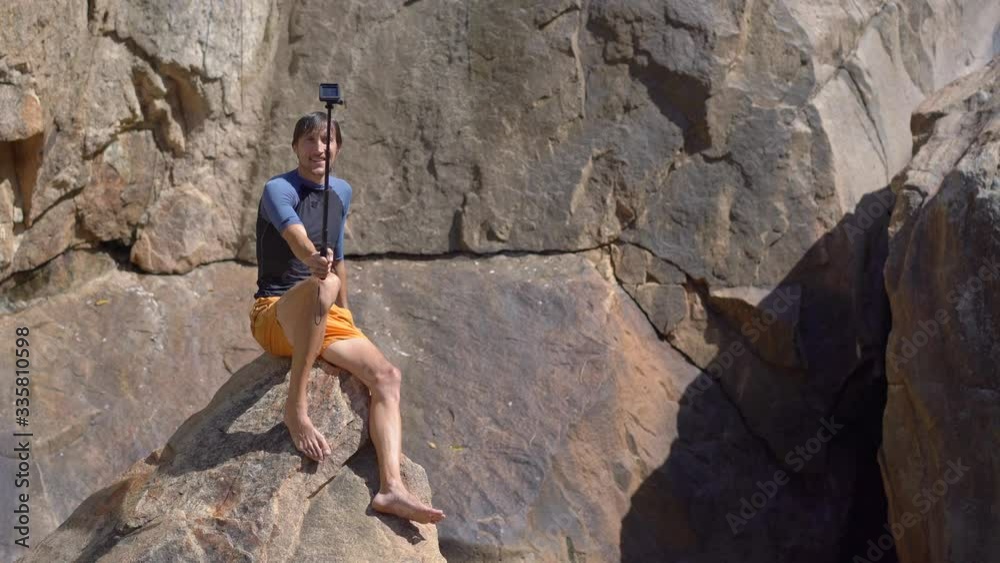 A young man sitting on the edge of a cliff making a selfie video