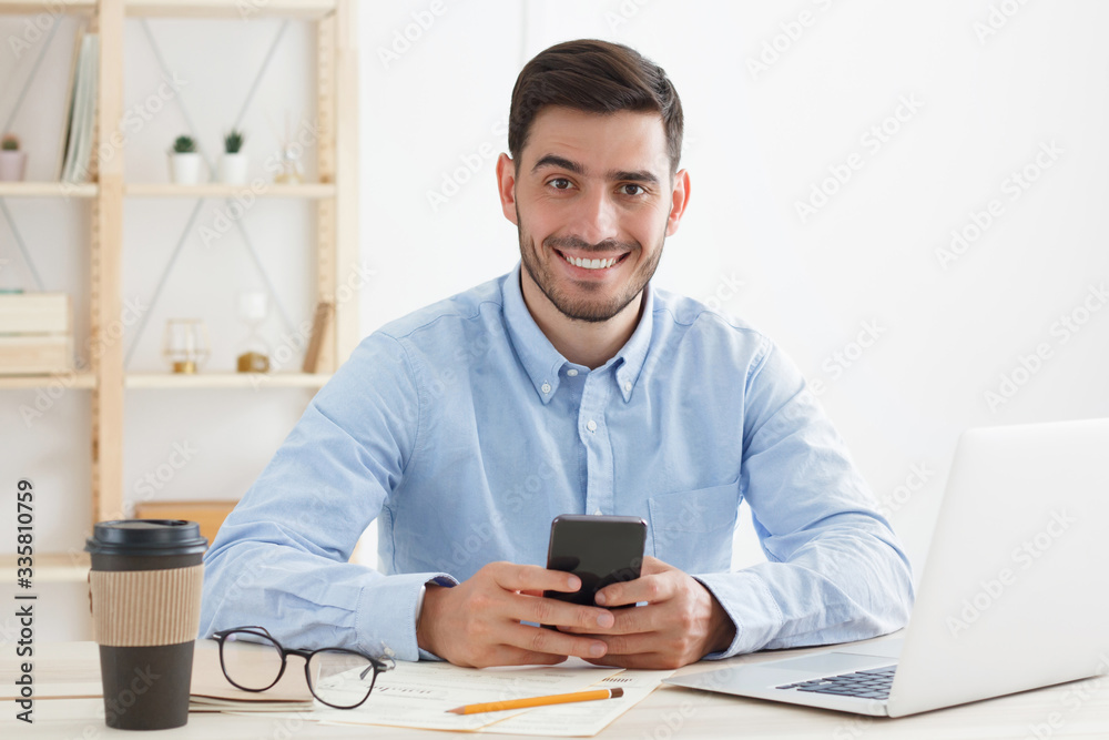 Young confident man spending lunch break in office, having rest from work while reading funny messages from friends and colleagues, smiling at camera Young confident man spending lunch break in office, having rest from work while reading funny messages from friends and colleagues, smiling at camera