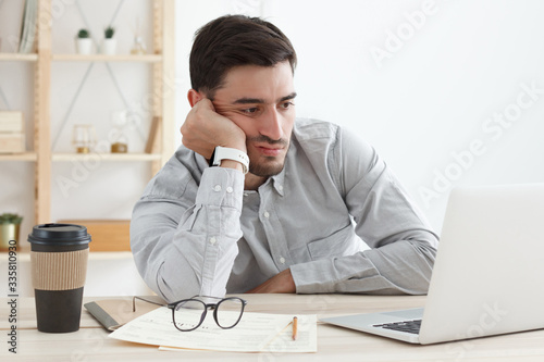 Business man in his office working on laptop, resting head on hand because he is tired, doing work overtime, stressed and bored photo