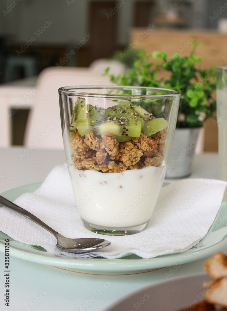 Glass of yogurt with granola and fruit kiwi in a green plate with restaurant background vertical Glass of yogurt with granola and fruit kiwi in a green plate with restaurant background vertical