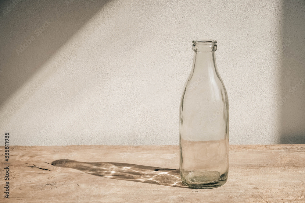 Glass transparent bottle on wooden table on white wall background. Copy, empty space for text Glass transparent bottle on wooden table on white wall background. Copy, empty space for text