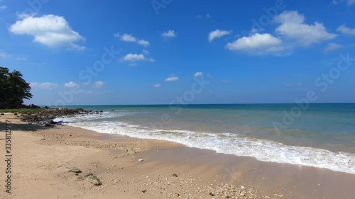 Beautiful white sand Phra Ae long beach of Koh Lanta island, Krabi, Thailand. Small waves splattering and splashing on rocky coast of sandy beach. Sunny day with clouds in sky.