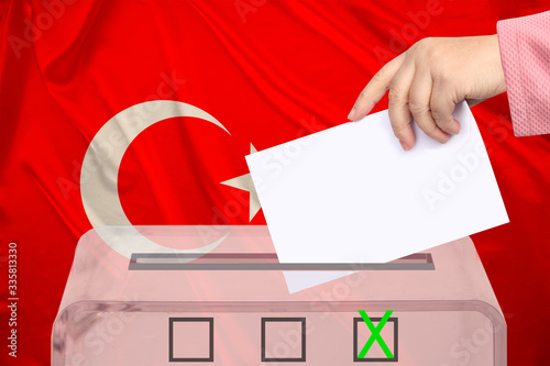 female voter lowers the ballot in a transparent ballot box against the background of the national flag of Turkey, concept of state elections, referendum