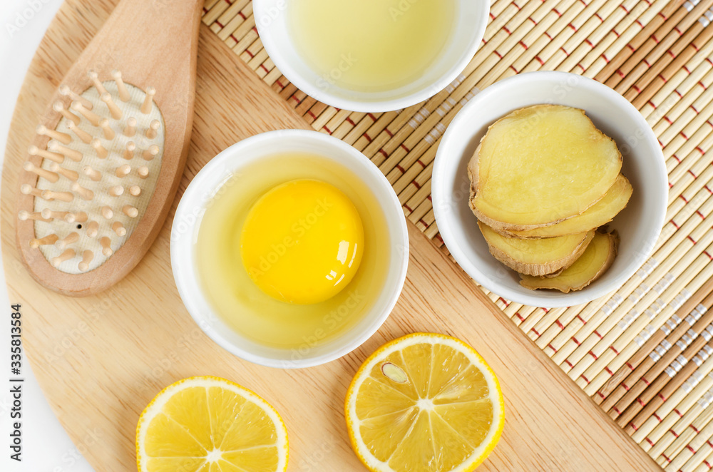 Raw egg in the small white bowl, wooden hair brush, lemon juice, lemon and ginger slices. Natural homemade hair treatment and zero waste concept. Top view, copy space Raw egg in the small white bowl, wooden hair brush, lemon juice, lemon and ginger slices. Natural homemade hair treatment and zero waste concept. Top view, copy space