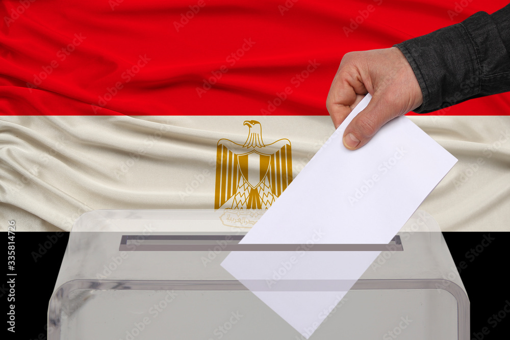 Obraz premium male voter drops a ballot in a transparent ballot box against the background of the national flag of Egypt, concept of state elections, referendum