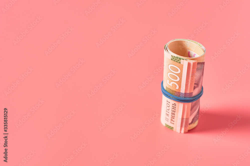 Roll of ukrainian money with rubber band on pink background. Payment of pensions, salaries. Bank loan. Business concept Roll of ukrainian money with rubber band on pink background. Payment of pensions, salaries. Bank loan. Business concept